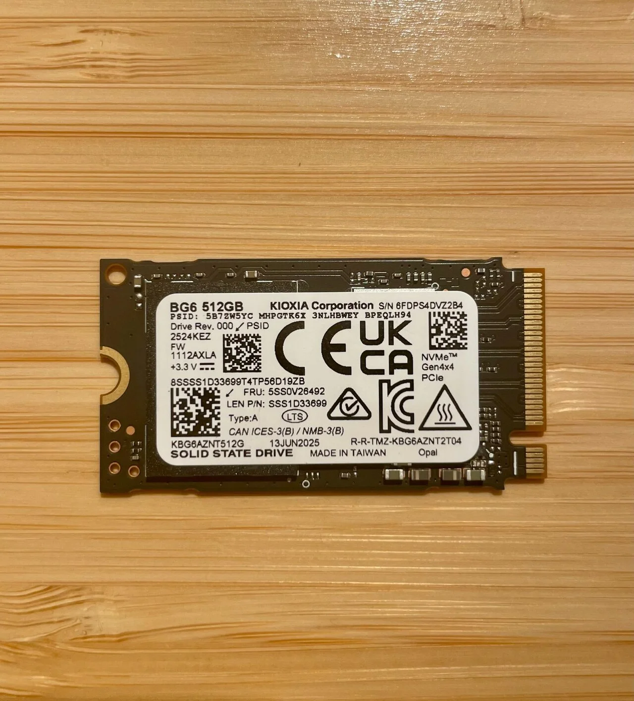 木目の台の上に置かれた細長い基板のSSD。白いラベルにBG6 512GB、KIOXIA Corporation、SOLID STATE DRIVE、NVMe Gen4x4 PCIeなどの文字が並ぶ